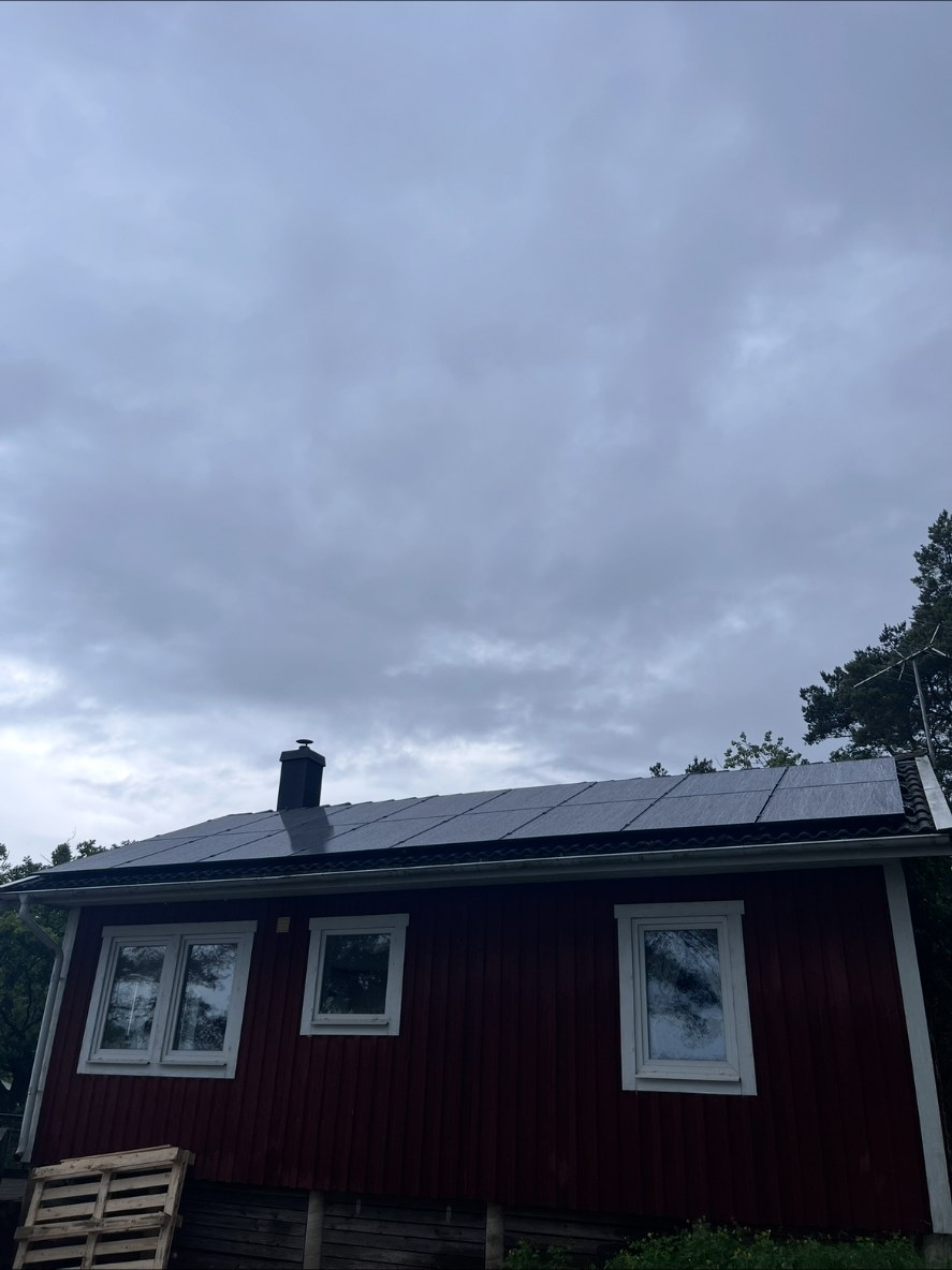 Solcellspaneler i en lång rad på det mörka taket till ett rött sommarhus i Nyköping