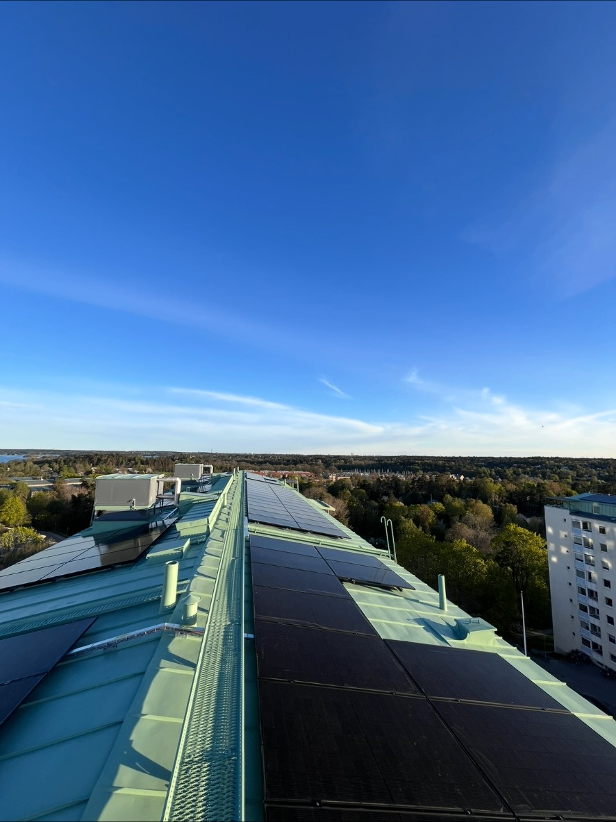 Solcellspaneler på grönt plåttak med en annan huskropp med balkonger i bakgrunden, bostadsrättsförening i Stockholm